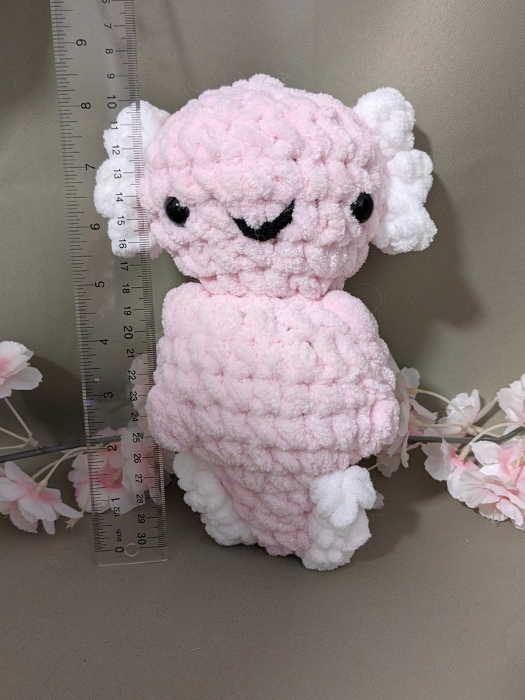 Chunky crochet axolotl plushie standing next to a ruler for size