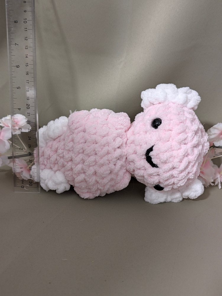Pink chunky crochet axolotl plushie lying on its side next to a ruler