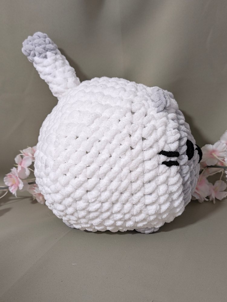 Back three-quarter view of the white crochet loaf cat plushie with a grey-tipped tail