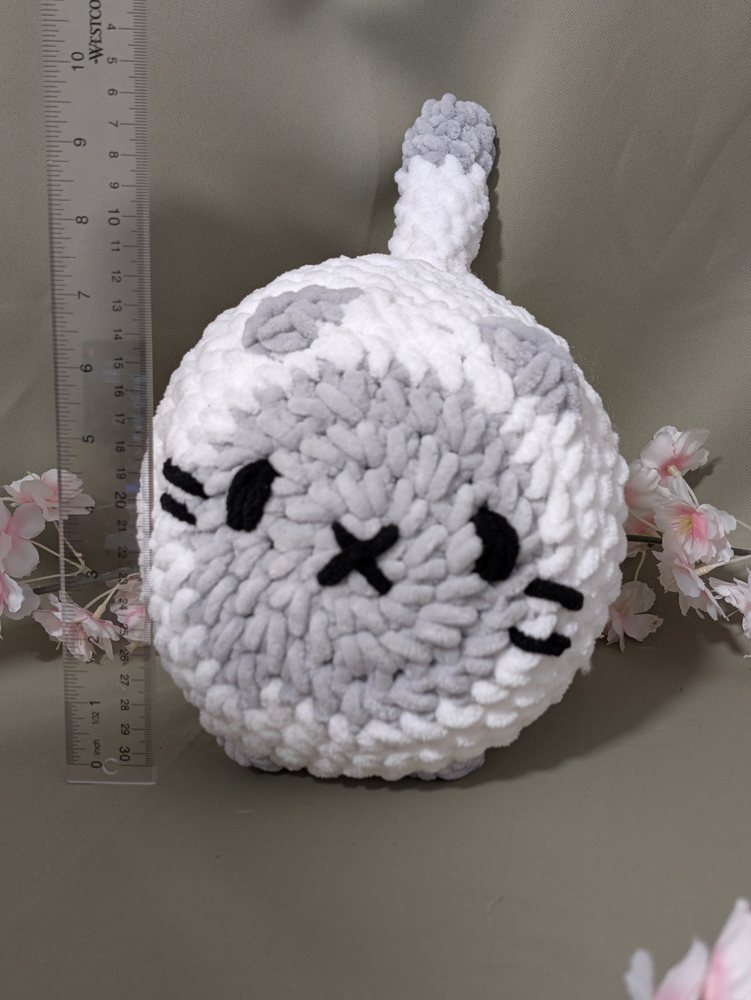 Front view of the crochet loaf cat plushie next to a ruler for size