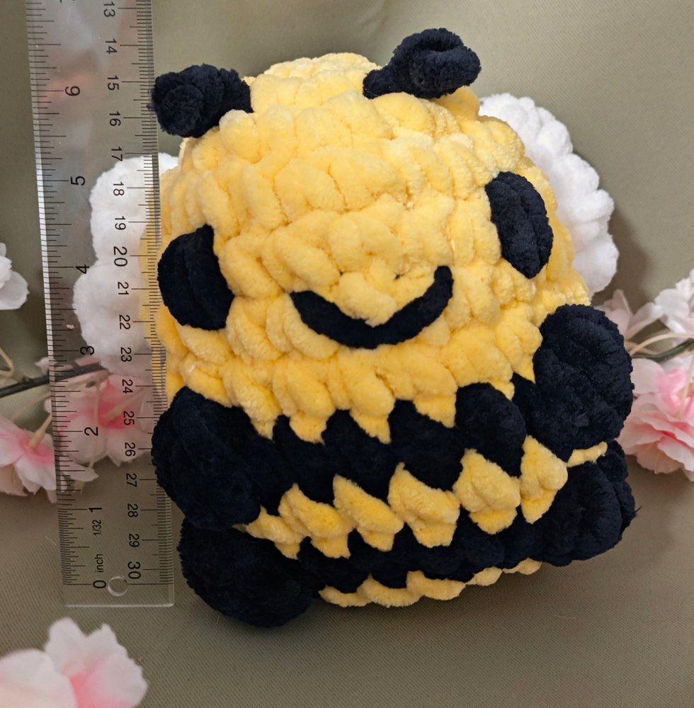 Three-quarter view of the crochet sitting bee plushie next to a ruler for size