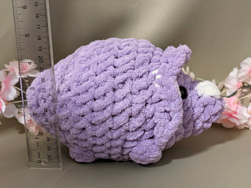 Side view of the purple crochet triceratops plushie next to a ruler for size