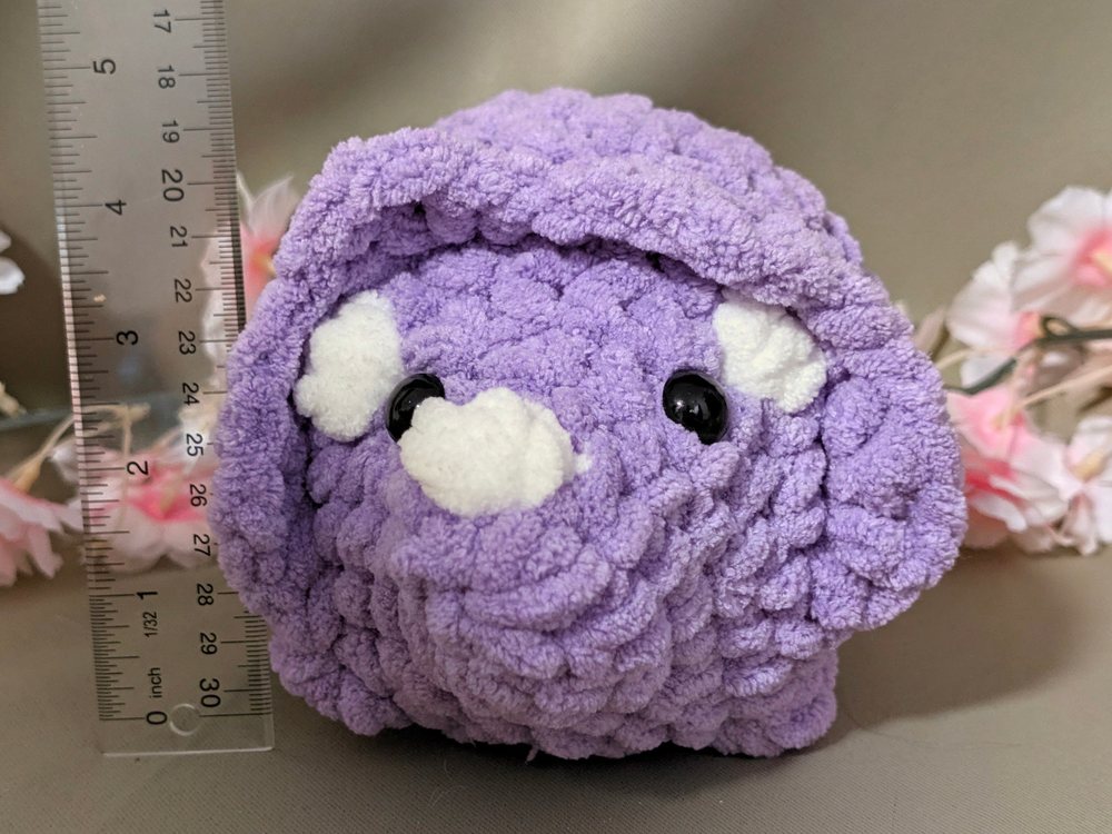 Front view of the purple crochet triceratops plushie next to a ruler